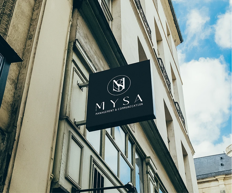 A black MYSA blade sign projecting from the stone facade of a classic European street building